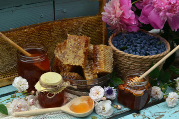 Still life with natural honey, honeycomb cut in pieces and honeysuckle berry with flowers on wooden background outside. Countryside summer rural background, vintage concept, healthy food