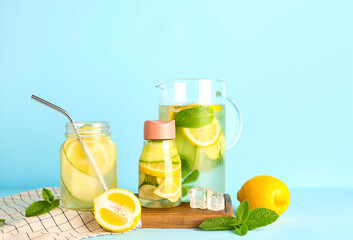 Sports bottle and jug of lemonade with cucumber on blue background
