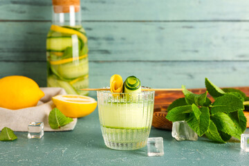 Glass and bottle of lemonade with cucumber on blue table