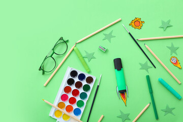 Creative composition with paper rocket, eyeglasses and different stationery on green background
