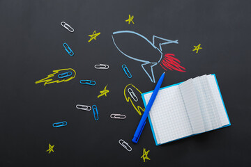 Creative composition with drawn rocket and different stationery on black chalkboard
