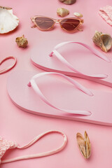 Pink flip-flops with swimsuit, sunglasses and shells on color background