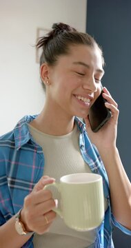 Vertical video of smiling biracial teenage girl with tea talking on smartphone, slow motion