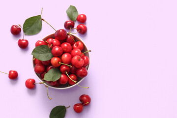 Bowl with sweet cherries and leaves on lilac background
