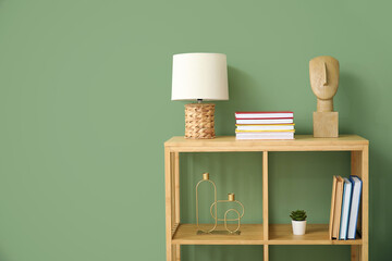 Shelving unit with lamp, books and decor near green wall in room - obrazy, fototapety, plakaty