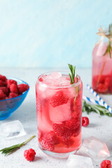 Glass and bottle of fresh raspberry lemonade with rosemary on white table