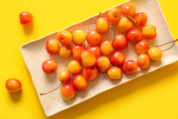 Plate with sweet yellow cherries on yellow background