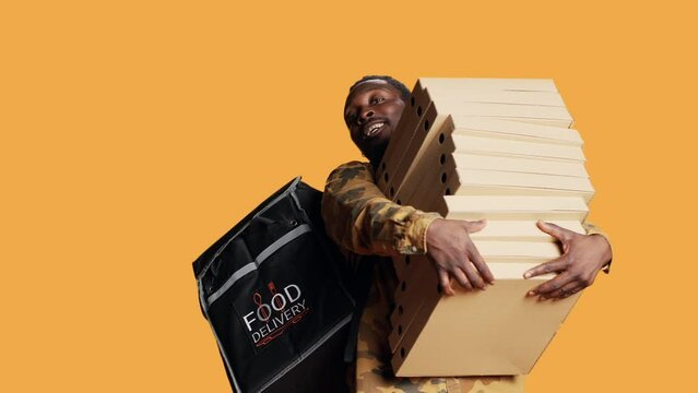 Young deliveryman giving huge stack of pizza boxes to client, delivering big fast food order and carrying takeaway backpack. Male model posing as delivery person with takeout food.