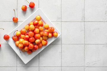 Plate with sweet yellow cherries on white tile background