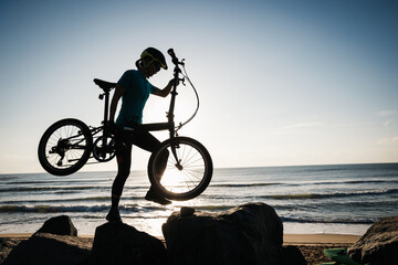 Fototapeta premium Woman taking a folding bike on sunrise seaside