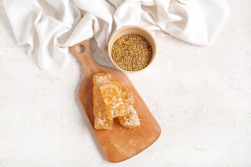 Wooden board with fresh honeycombs and bee pollen on light background