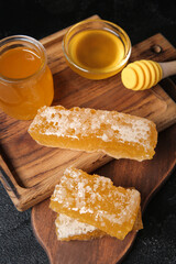 Wooden board with fresh honey and combs on dark background, closeup