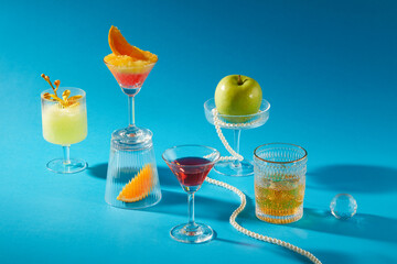 Many delicious drinks glasses are decorated on a blue background: whiskey, cocktail and smoothie glasses with glass ball and pearl necklace. Scene for advertising, front view