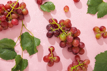 Tasty ripe grapes with leaves in water on pink background