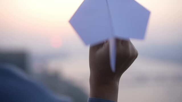 young female flying paper plane at sunset