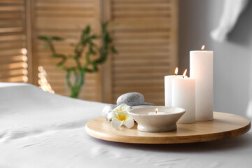 Fototapeta na wymiar Burning candles with stones and flowers on couch in spa salon, closeup