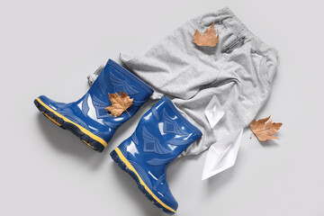 Blue gumboots with trousers, paper ships and autumn leaves on grey background