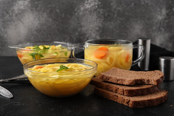 Bowl and pots of tasty chicken soup with bread on table against grey background
