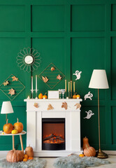 Fireplace with Halloween pumpkins and autumn leaves near green wall