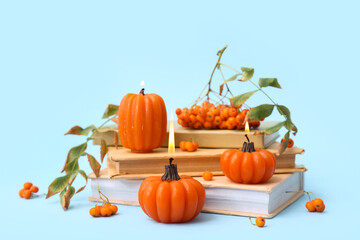Beautiful autumn composition with burning candles in shape of pumpkin, books and rowan berries on blue background
