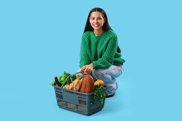 Young woman with shopping basket on blue background