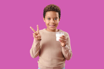 Little African-American boy with glass of milk showing victory gesture on purple background