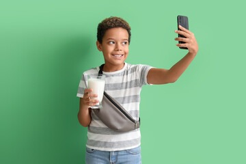 Little African-American boy with glass of milk taking selfie on green background - obrazy, fototapety, plakaty