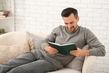 Handsome man reading book on sofa in living room