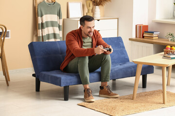 Obraz premium Handsome man playing video game on sofa in living room