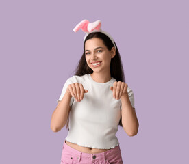 Obraz na płótnie Canvas Happy young woman with bunny ears on lilac background