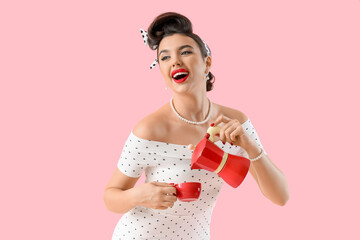 Young pin-up woman with geyser coffee maker and cup on pink background