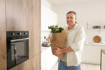 Mature man with paper bag of fresh vegetables in kitchen