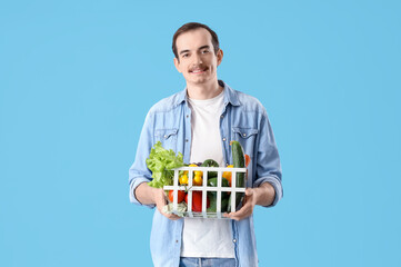 Young man with basket of fresh vegetables on blue background