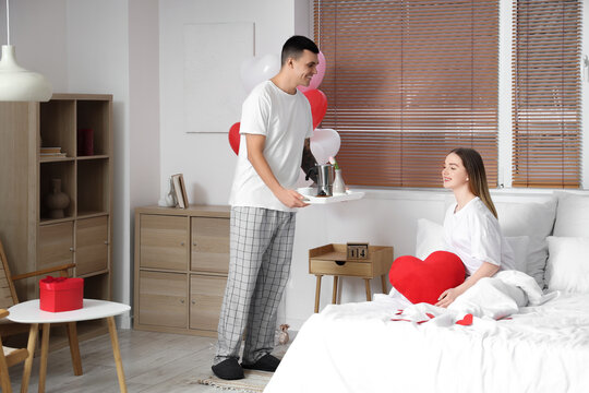 Young man bringing his beautiful wife breakfast in bed on Valentine's Day