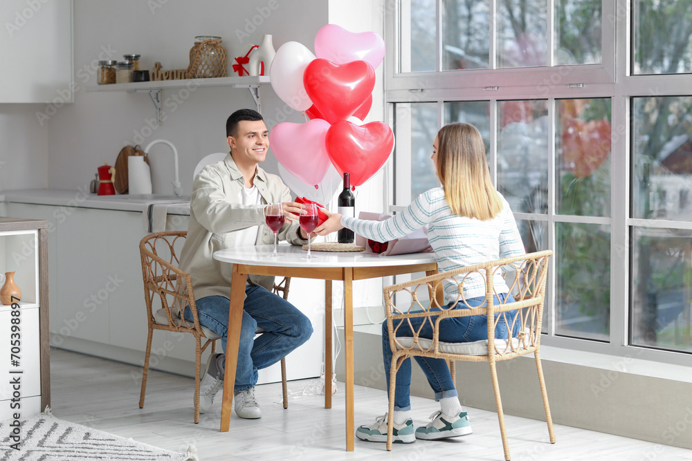 Poster Beautiful young couple with glasses of wine and gift box celebrating Valentine's Day at home