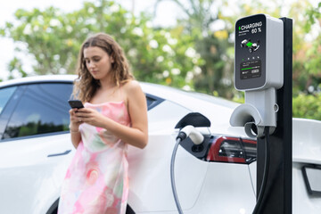 Modern eco-friendly woman recharging electric vehicle from EV charging station. Innovative EV...