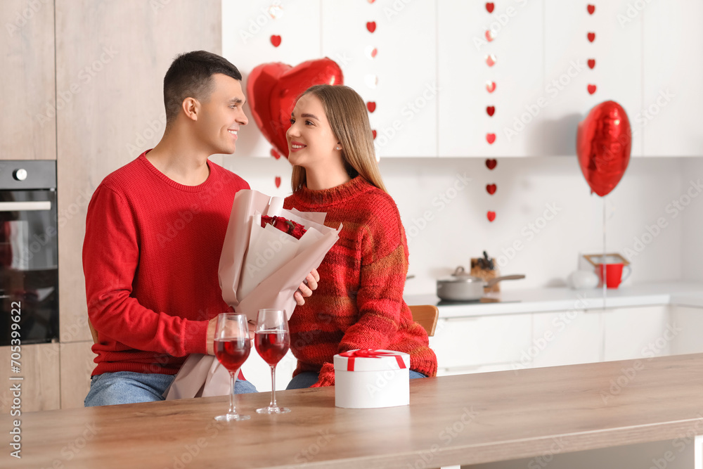 Wall mural Beautiful young couple with bouquet of roses, gift box and wine glasses celebrating Valentine's Day at home