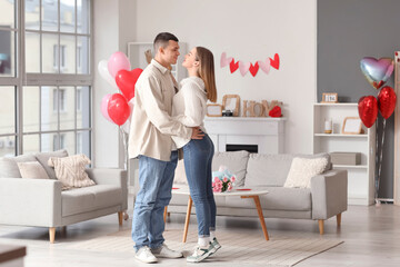 Beautiful young couple with heart-shaped balloons hugging and celebrating Valentine's Day at home