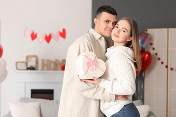 Beautiful young couple with gift box hugging and celebrating Valentine's Day at home