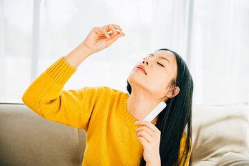 An Asian woman uses a self COVID-19 rapid antigen test inserting a swab into her nose at home. Emphasizing virus prevention testing and pandemic protection.