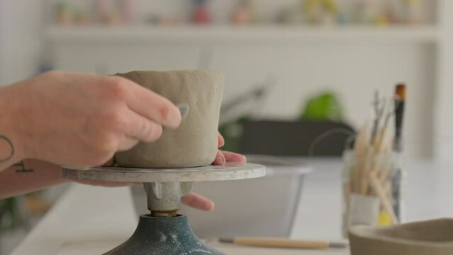 Working designs into soft clay with a specialized tool, showcasing artisan's delicate touch