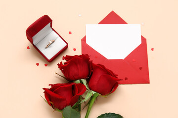 Box with beautiful engagement ring, envelope and red roses on beige background