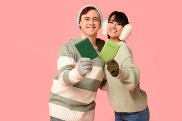 Beautiful young happy couple with passports on pink background. Winter vacation concept