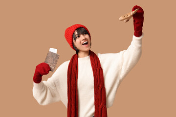 Beautiful young happy woman with wooden airplane, passport and ticket on brown background. Winter vacation concept