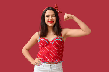 Beautiful young happy pin-up woman showing muscles on red background