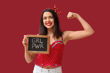 Beautiful young happy pin-up woman holding blackboard with text GIRL POWER and showing muscles on...