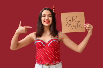 Beautiful young happy pin-up woman pointing at paper sheet with text GIRL POWER on red background