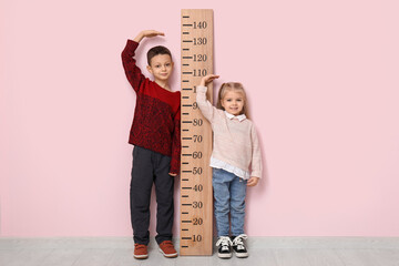 Cute little children measuring height near pink wall - obrazy, fototapety, plakaty