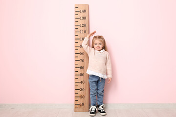 Cute little girl measuring height near pink wall