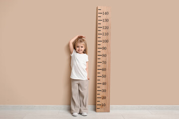 Cute little girl measuring height near beige wall - obrazy, fototapety, plakaty